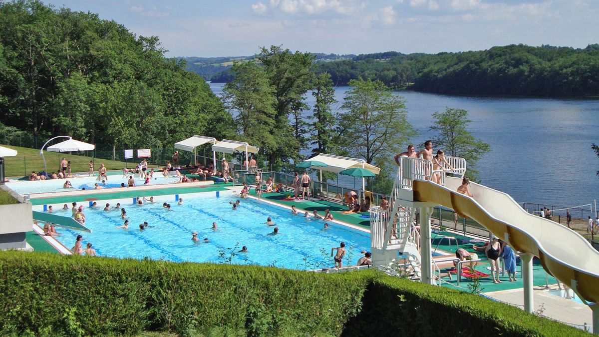 Grand bassin de la piscine de Saint-Etienne-Cantalès dans le Cantal, son toboggan et sa vue sur le lac de barrage